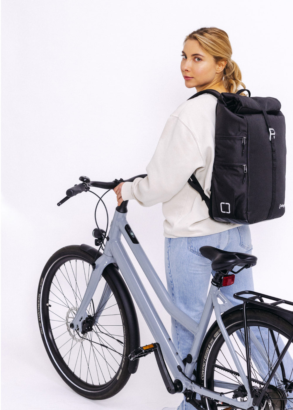 Wasserdichter otinga Flip V2 in schwarz Rucksack und Fahrradtasche mit Frau die neben Fahrrad steht und Rucksack auf dem Rücken trägt 