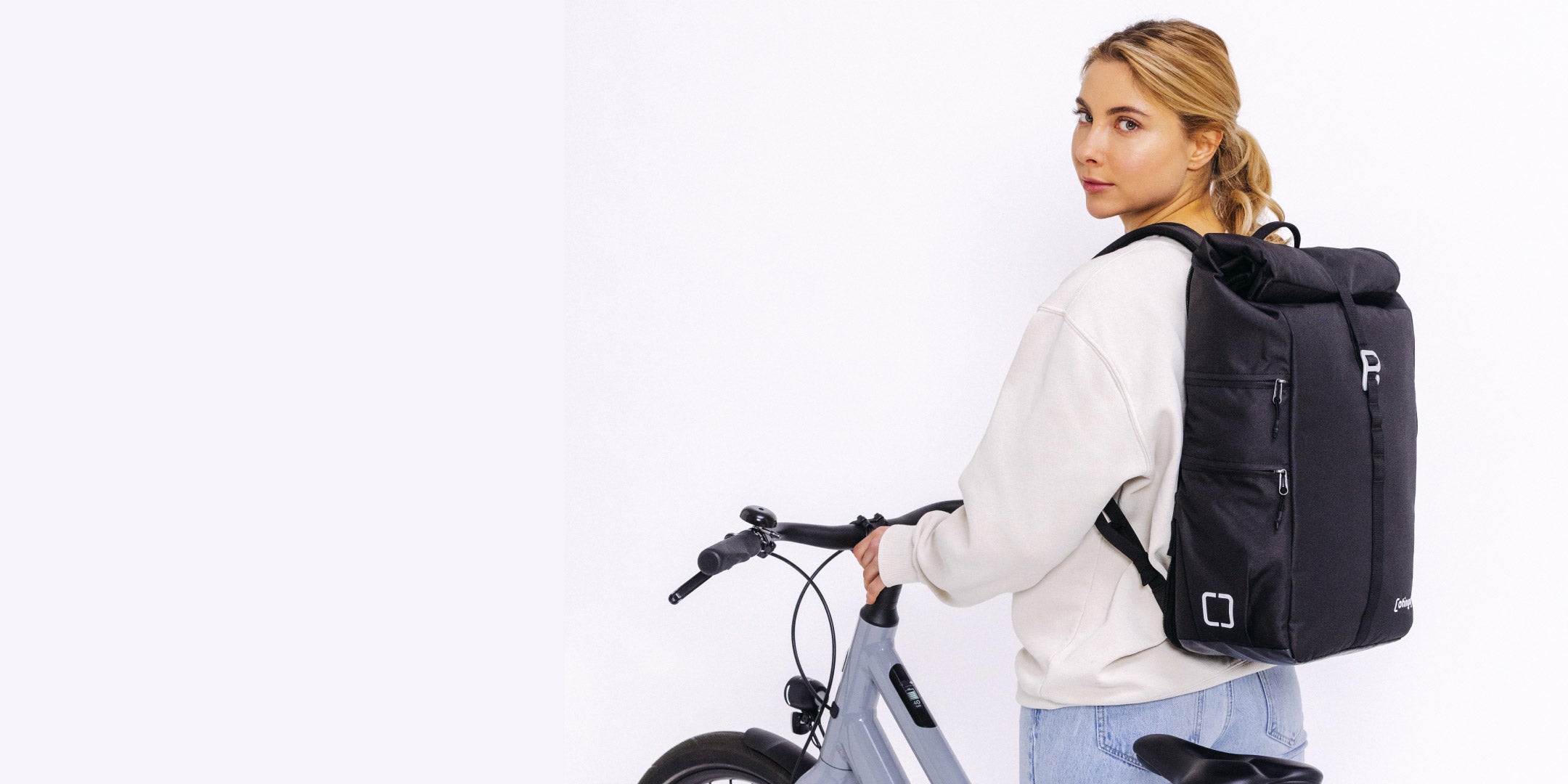 Wasserdichter otinga Flip V2 in schwarz Rucksack und Fahrradtasche mit Frau die neben Fahrrad steht und Rucksack auf dem Rücken trägt 