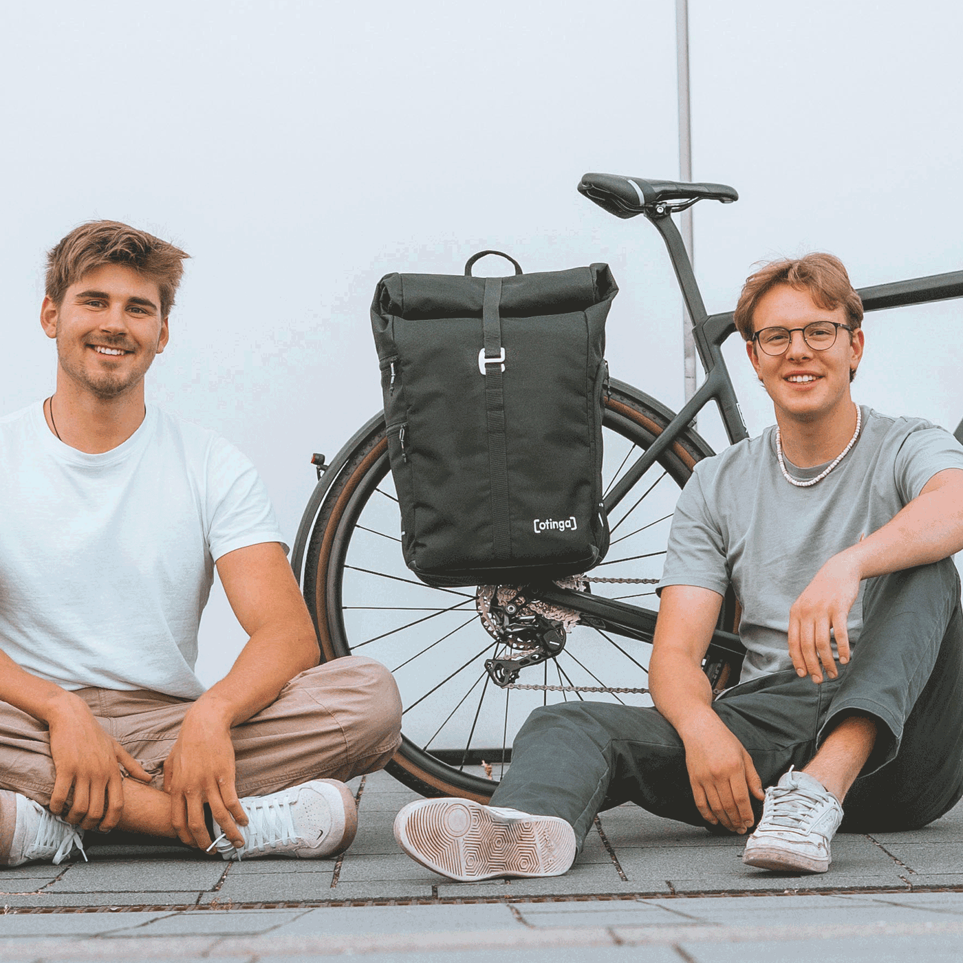 Leander Mellies und Karl Fischer (Aachen, Berlin) die Gründer von otinga / 2bag mit dem Flip / 2bag Rucksack und Fahrradtaschen Kombination auf dem Boden sitzend vor einem Fahrrad
